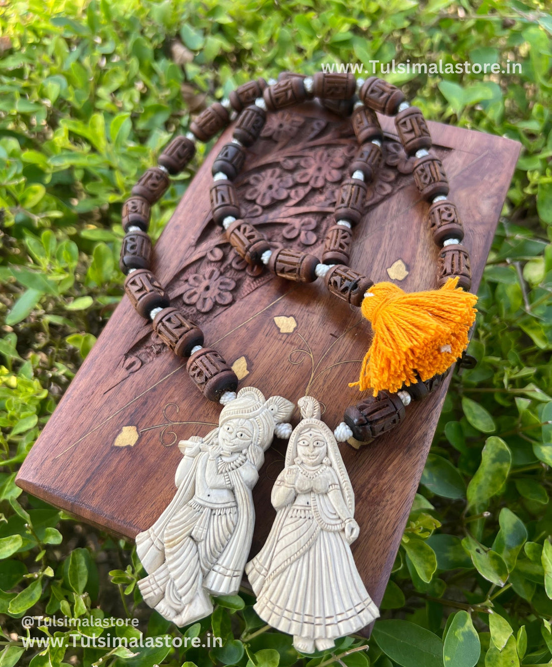 Carved dark tulsi mala with orange tassel and white Radha Krishna figure pendants