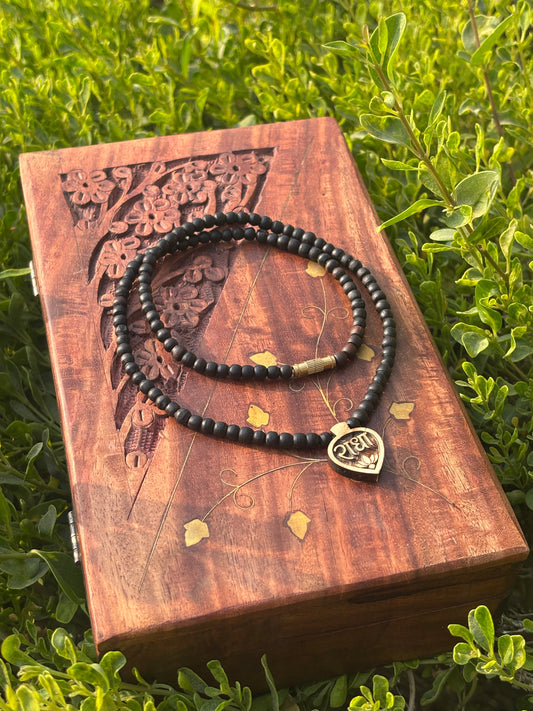 Black tulsi bead mala with leaf-shaped Radha locket on a carved wooden box