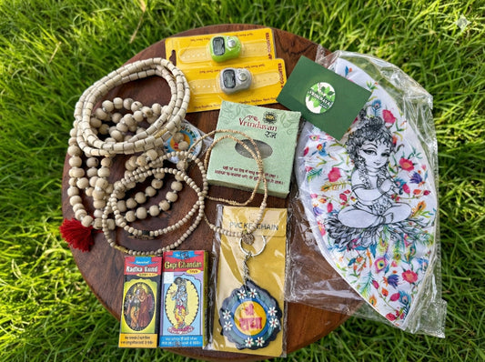 Bhakti kit spread on grass — tulsi malas, japa counters, tilak packets and a Krishna print