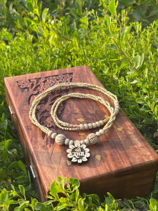 Cream tulsi mala with Shri Radha flower locket on a carved wooden box in greenery