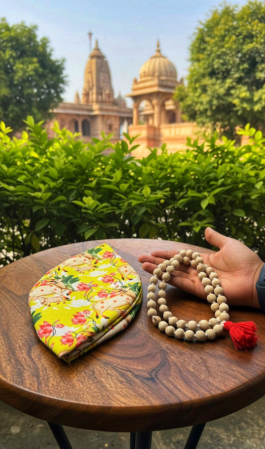 Tulsi japa mala with red tassel beside a floral japa bag on a wooden table