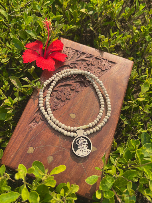 Tulsi mala with round carved locket on a wooden box beside a red hibiscus flower