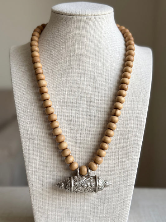 Brown round tulsi bead kanthi mala with silver Bhaktamal kavach pendant on a linen bust